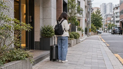 A traveler checking a phone beside a suitcase on a city sidewalk