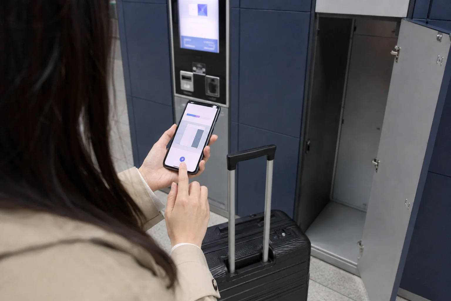 Visitor using a phone beside an open subway luggage locker and carry-on